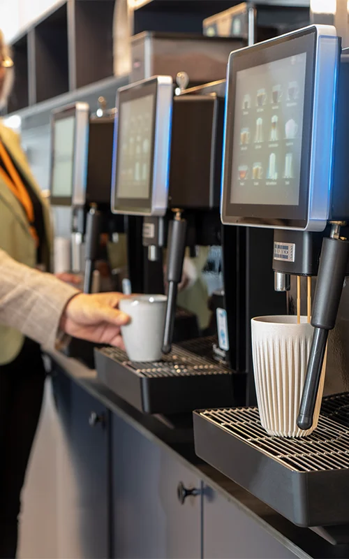 Kaffemaskiner der brygger kaffe med mennesker i baggrunden